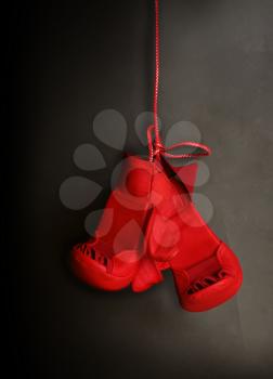 A pair of children's red karate gloves hang on a dark gray background