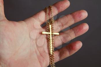 man's hand holds a metal cross on a chain close-up