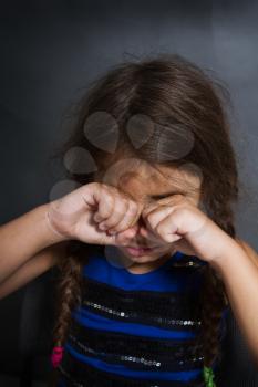 a little girl with two pigtails sits and weeps bitterly on a grubby gray background
