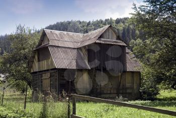 Old wooden abandoned house with boarded up windows against the background of the green Carpathian Mountains