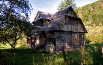 Old wooden abandoned house with boarded up windows against the background of the green Carpathian Mountains