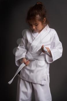 Little girl karatek in a kimono tie a white belt getting ready for training