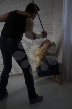 Domestic violence. An aggressive man beats a girl who hides in a corner and tries to avoid blows