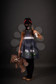One teenage girl hooligans in bright smart dress, but in gangster balaclava hats with heavy clubs posing on a gray background with their favorite toy bear