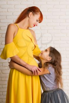 The little girl gently pressed and hugs her mom in a bright dress