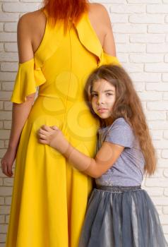 The little girl gently pressed and hugs her mom in a bright dress