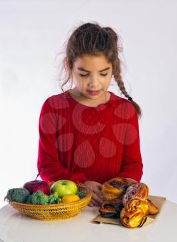Little girl chooses what to eat, healthy food or buns