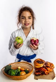 A little girl in karate uniform and a blue belt chose apples to eat instead of bread rolls.