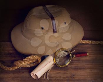 a still life with an old battered cork helmet with a folded map and a rope on a wooden background.