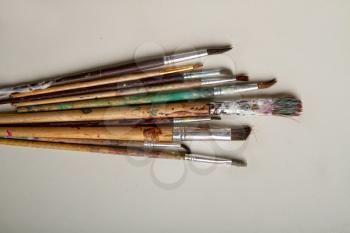 Old used dirty brushes of different sizes on a scratched yellowish surface