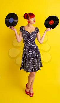 Pretty girl in retro dress in polka dot holding vinyl discs on a bright yellow background