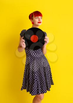Pretty girl in retro dress in polka dot holding vinyl disc on a bright yellow background