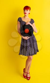 Pretty girl in retro dress in polka dot holding vinyl disc on a bright yellow background