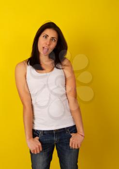 Pretty girl with dark hair in casual clothes in good mood makes a wry face and makes a face on a bright yellow background
