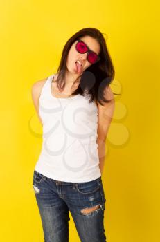 Emotional comely young girl grimacing in pink sunglasses on bright yellow background in casual clothes