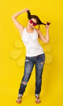Emotional comely young girl grimacing in pink sunglasses on bright yellow background in casual clothes