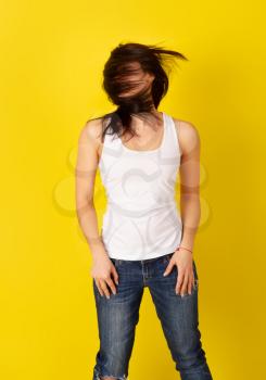 Pretty girl with dark hair in casual clothes in good mood is indulging with her hair on a bright yellow background