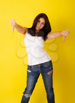 Young pretty girl in casual clothes shows thumbs down in a disapproving gesture on bright yellow background
