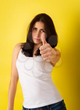Young cute girl in casual clothes shows a thumbs up in an approving gesture on a bright yellow background