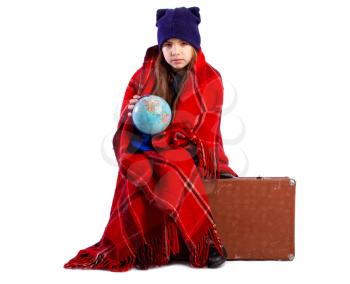 Little frozen girl wrapped in a blanket and hat sitting on a suitcase and exploring the globe plan to go in warmer climates