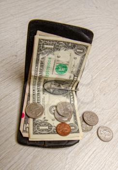 an old leather wallet of a very not rich person with a few small dollar bills and coins lying next to each other on a dirty background.