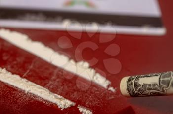 plastic card, cocaine poured in tracks and a one-dollar bill rolled up into a tube for taking the drug on a dark red surface close-up