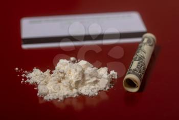 plastic card, cocaine in a handful and a dollar bill rolled up into a tube for taking the drug on a dark red surface close-up