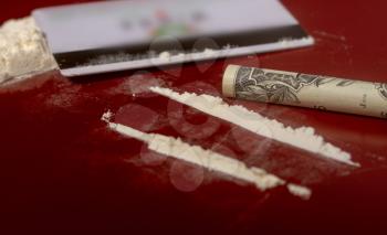 plastic card, cocaine poured in tracks and a one-dollar bill rolled up into a tube for taking the drug on a dark red surface close-up