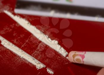 plastic card, cocaine poured in tracks and a Ukrainian bill of ten hryvnia rolled into a tube for taking the drug on a dark red surface close-up