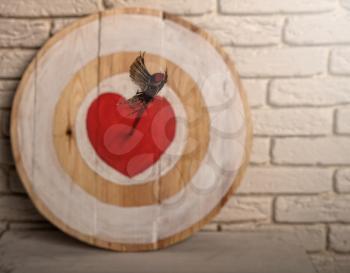 Handmade rough wooden target with a center in the form of a red heart and an arrow from a bow that hit the center