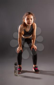 little tired girl in sportswear drinks water and rests after a workout on a dark background