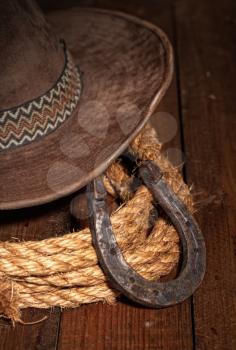 An old horseshoe lies next to a classic cowboy hat and lasso on a dark wooden background.
