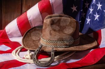 Classic cowboy hat lasso and horseshoe lie on a star-striped USA flag on a dark wooden background
