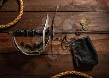 Lying on a wooden table Old pirate sword next to a few small purses with a purse and rope