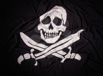 traditional waving pirate flag jolly roger skull with two crossed sabers on dark fabric background