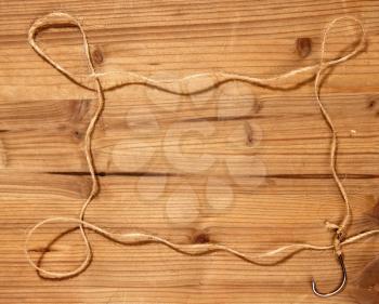 A large classic fishing hook with a coarse rope tied to it forms a simple frame on a wooden background