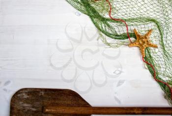 old white wooden boards on top of which lies a fishing net with starfish and an oar. With place for your text.