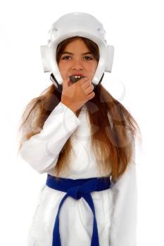 A karate girl in a protective helmet with a blue belt and a white kimono puts on a mouth guard and prepares for training