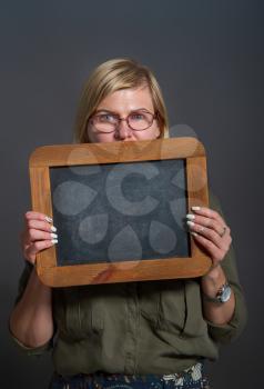Adult woman holding a blank chalk board on a dark background
