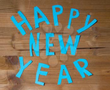 Happy New Year inscription casually cut out by scissors from blue paper laid out on a wooden background