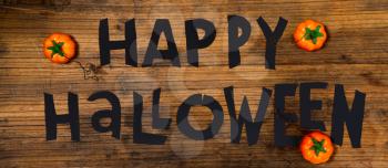 Happy Halloween lettering carelessly scissored from black paper on a wooden surface next to small artificial pumpkins