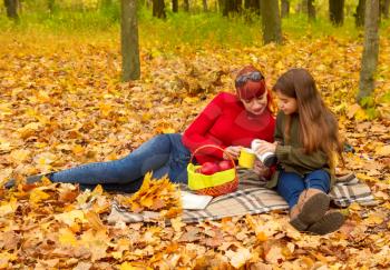 young mother and little daughters in bright sweaters on a picnic in nature drink tea from a thermos