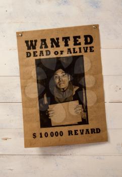 old paper announcement of criminal search and reward on yellowed paper pinned to a rough wooden wall