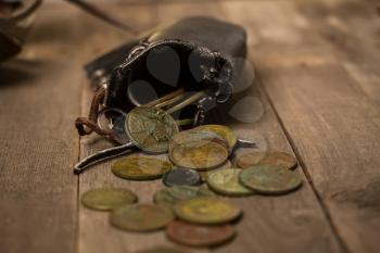 old black leather money bag and small copper coins of different countries coins next to it on a rough wooden table