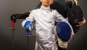 athlete and trainer mother and son in white traditional and black coaching protective fencing equipment with rapiers on a dark background