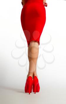 slim female legs in bright red high-heeled shoes and a red dress on a light background