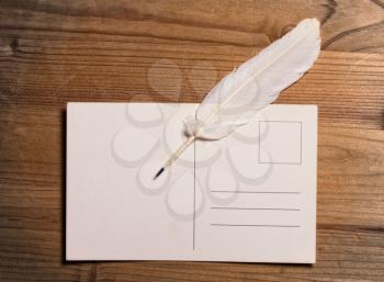 white writing pen lying on top of a clean old post card on a wooden surface