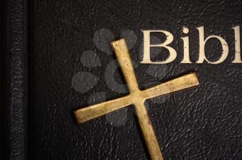 Holy Bible in a dark cover close-up and a metal brass cross lying on it
