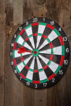 darts target hanging on an old wooden wall with a red arrow hitting her exactly in the center