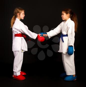 Two little karate women in white kimonos, one in red and the other in blue competition equipment shake hands as a sign of respect before the fight against a dark background